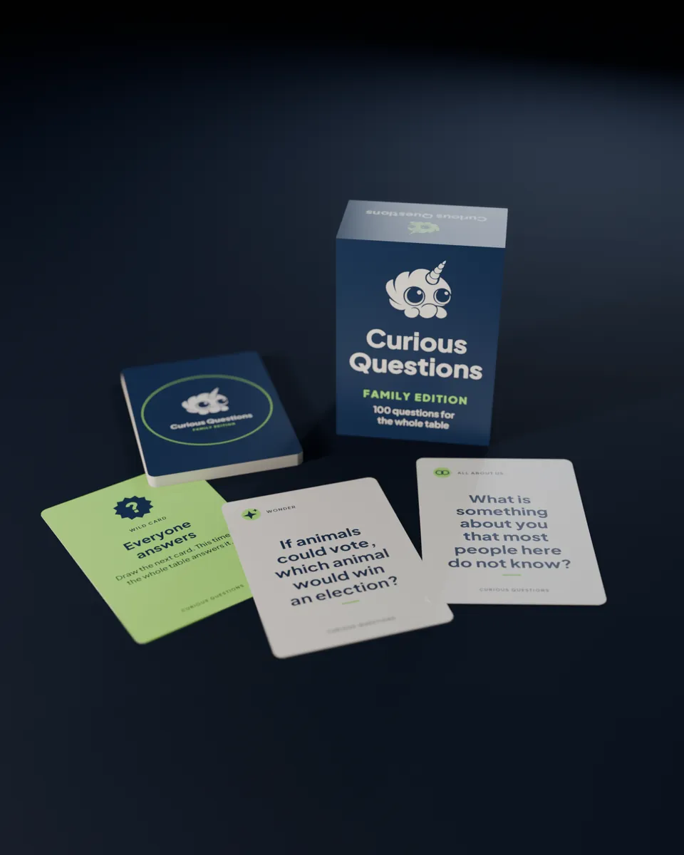 The Curious Questions box standing beside a face-down deck, with a wild card and two question cards dealt in front