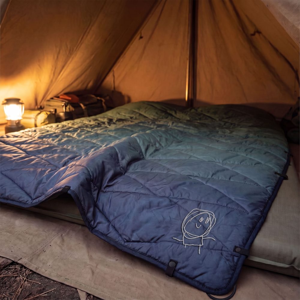 Puffer blanket in Arctic Glow, in a tent, with an example drawing stitched in the corner