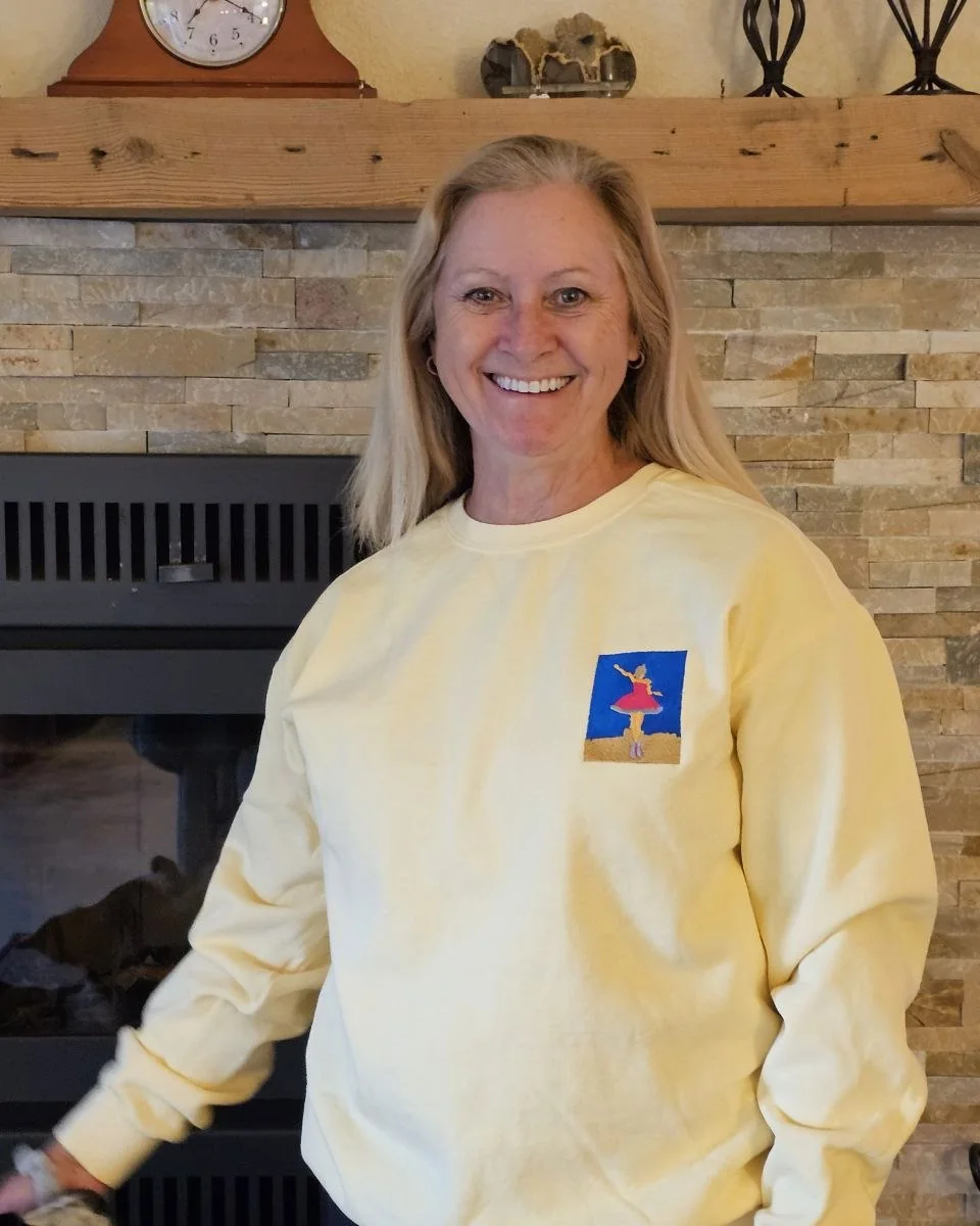 A woman wearing the butter-yellow sweatshirt, the ballerina embroidery stitched on the chest