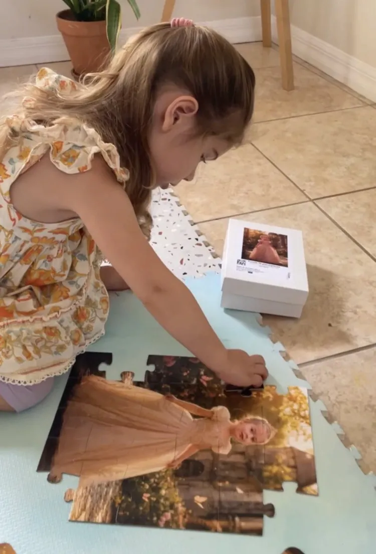 A young girl assembling her custom princess portrait puzzle on the floor beside its gift box