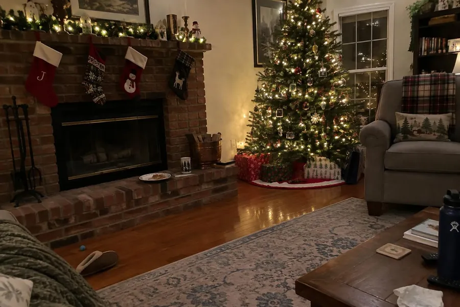 A family room with a brick fireplace, stockings and a tall Christmas tree
